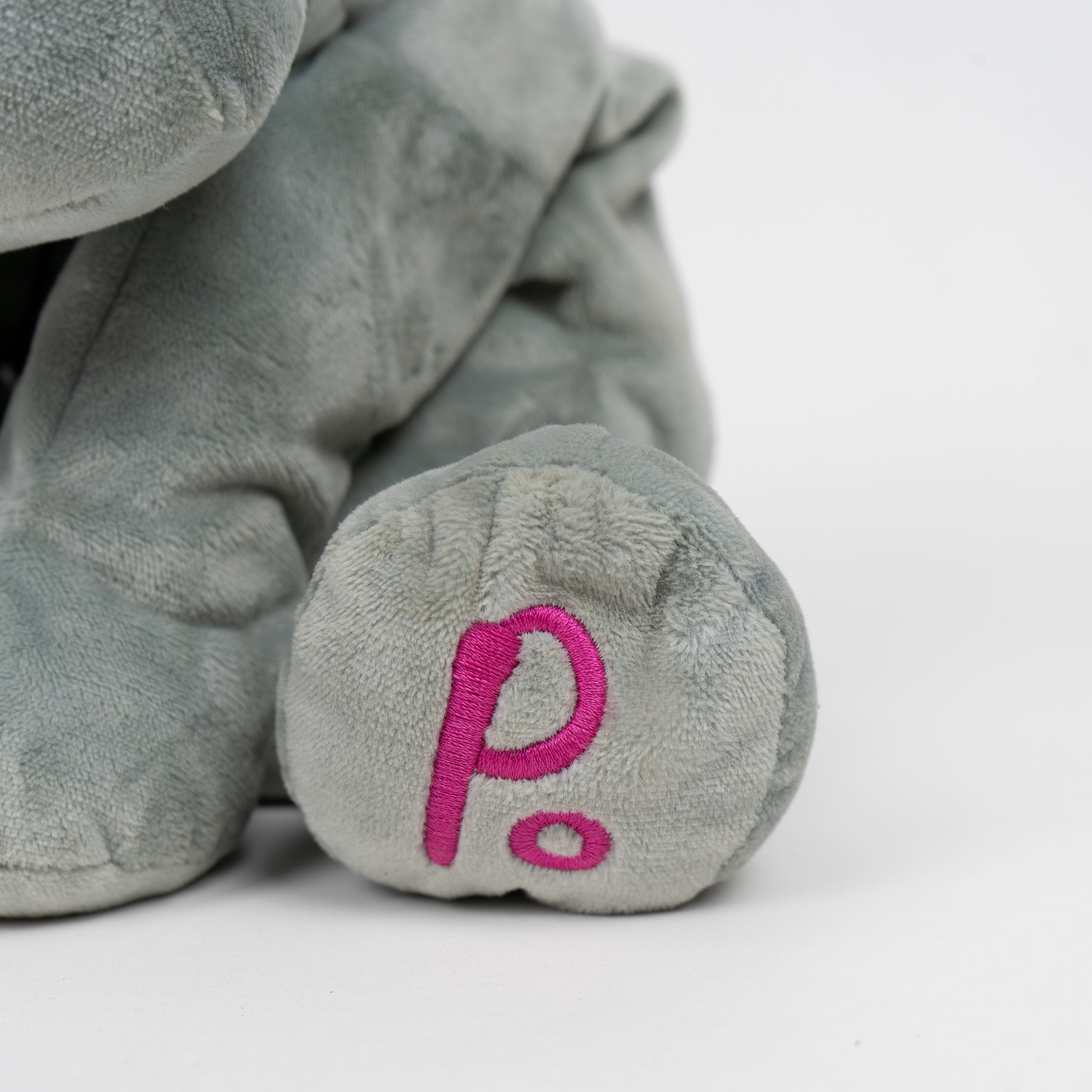 Gray plush toy with a pink 'PO.' on a white background