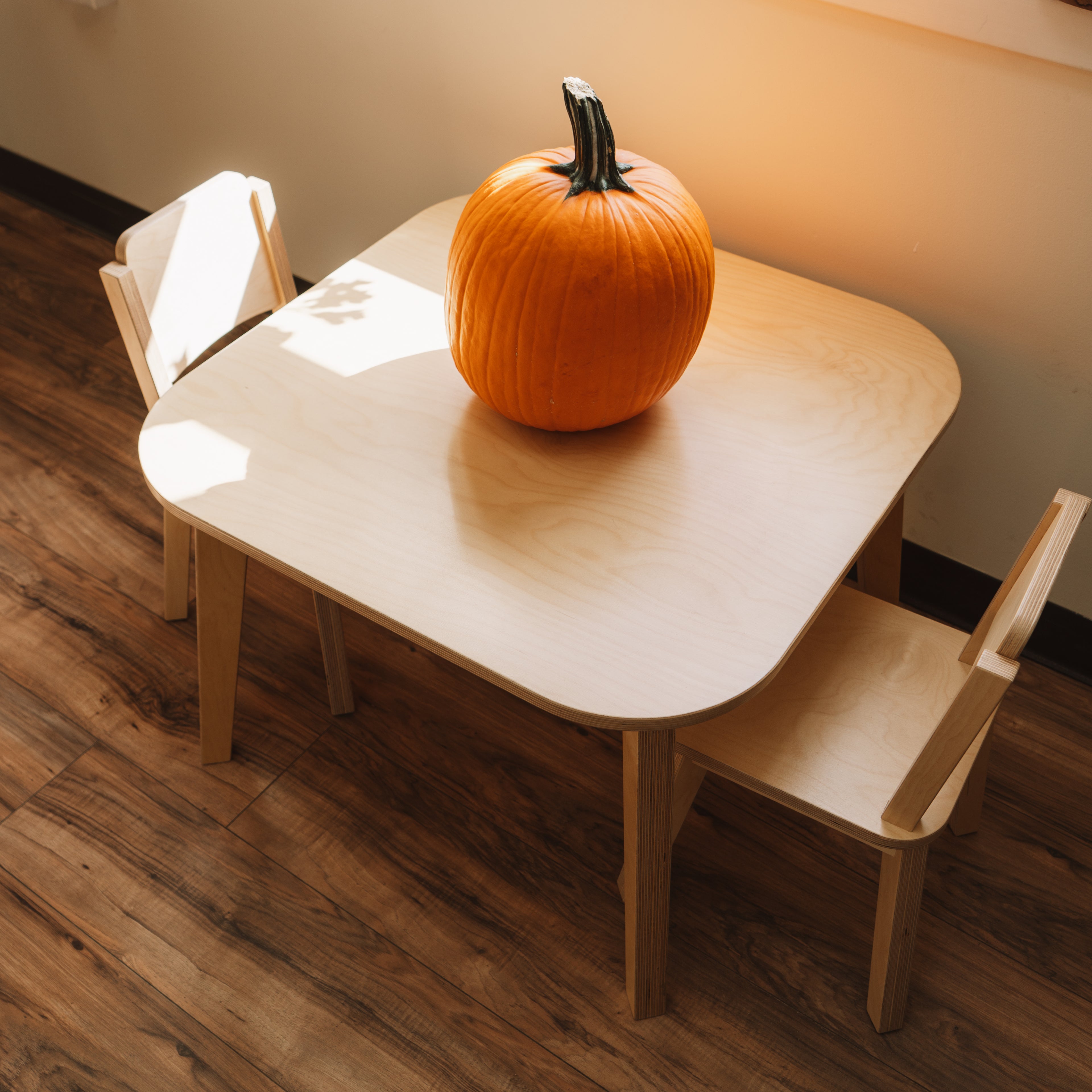Wooden children's table and chairs with a pumpkin on top in a room.