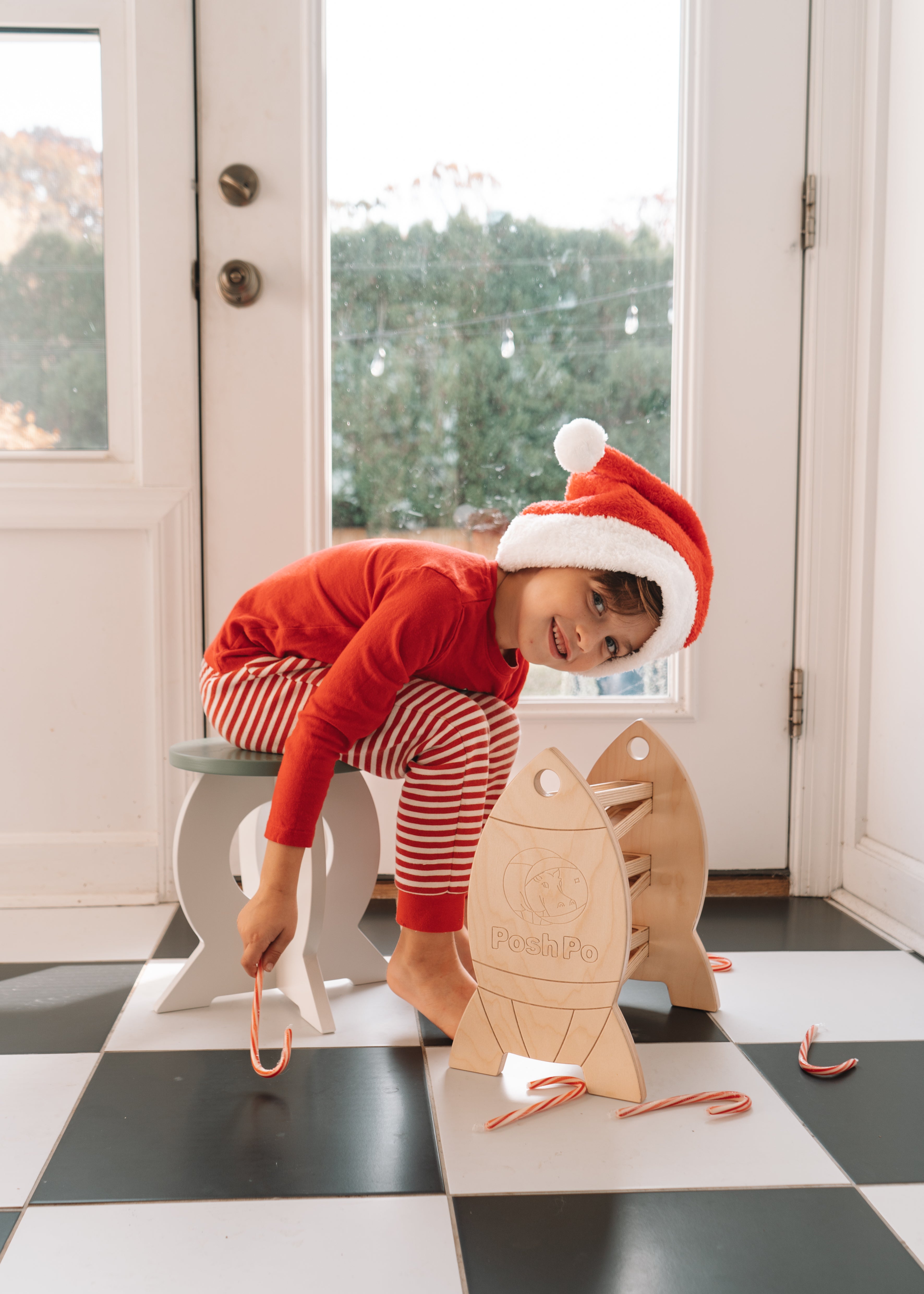 Child wearing a Santa hat playing with a wooden toy on a checkered floor.